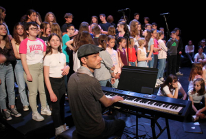 « L’artiste icaunais GEHEL plaque ses ultimes accords sur le piano permettant d’effectuer la balance sur la scène du théâtre d’Auxerre. A ses côtés, une centaine d’enfants se préparent à chanter. Les répétitions du Festival des chorales académiques bat son plein avant le récital du projet « Art et Culture » porté par Saint-Joseph-la-Salle ce soir… ».